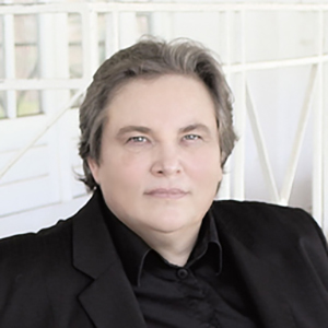 Eine Person mit kurzem grauem Haar in schwarzem Anzug blickt ruhig in die Kamera